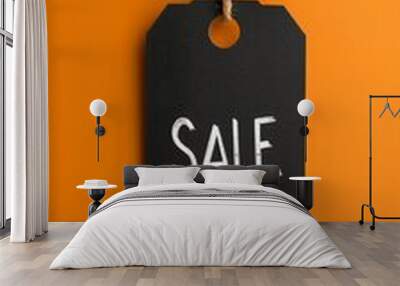 Black sale tag with white lettering hanging by twine against vibrant orange background, symbolizing retail discounts and promotional offers.Black Friday concept Wall mural