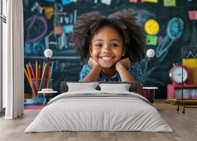 Cheerful young student with curly hair smiles brightly at her colorful desk, surrounded by school supplies and a chalkboard filled with doodles and notes. Wall mural