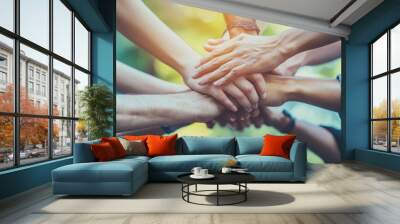 Diverse hands joining together in unity, symbolizing teamwork, collaboration, and community support against a vibrant, blurred natural background. Wall mural