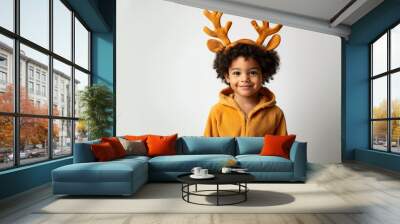 Festive child in yellow hoodie wearing reindeer antlers, smiling brightly against white background. Holiday cheer and innocence captured in portrait. Wall mural