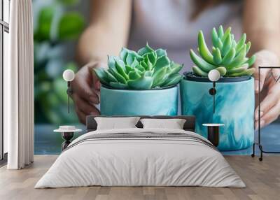 Hands gently cradle two vibrant blue ceramic pots housing lush green succulents, showcasing the beauty of indoor gardening and the art of plant parenthood. Wall mural