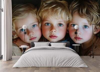 Three adorable blonde children with striking blue eyes gaze intently at the camera, their faces close together in a heartwarming portrait of sibling love and innocence. Wall mural