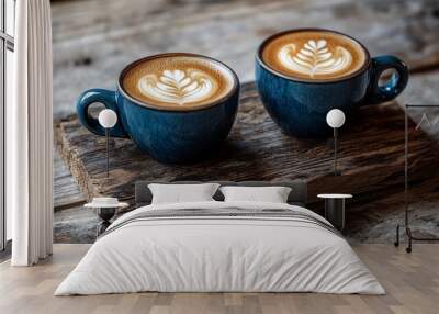 Two artfully crafted cappuccinos in deep blue ceramic cups sit side by side on a rustic wooden board, their creamy latte art designs inviting a moment of shared indulgence. Wall mural