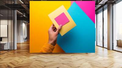 Vibrant geometric composition with hand holding yellow paper against colorful background, showcasing creative design and minimalist aesthetic in bold hues. Wall mural