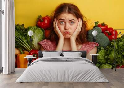 Woman with surprised expression surrounded by colorful vegetables on vibrant yellow background, conveying overwhelm with healthy eating choices. Wall mural