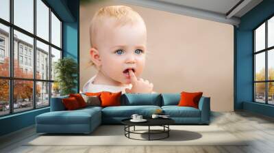 Portrait of blue-eyed baby sucking finger in her mouth, two first teeth are visible. Wall mural