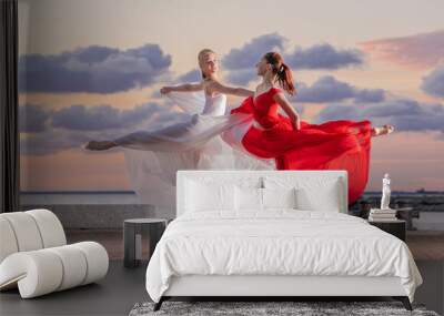 Two ballerinas in a white and red flying skirt and leotard dancing in a duet on the embankment of the ocean or sea against the backdrop of the sunset sky Wall mural