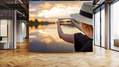 Pretty preteen girl in summer straw hat taking selfie for cellphone at beautiful sunset on lake, lifestyle, local travel concept, young blogger Wall mural