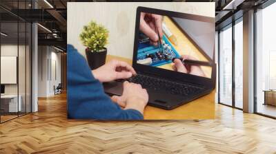 A man looks at a laptop online electronics repair courses. Soldering station with LED display, heating controller, with a soldering iron. Online learning concept. Wall mural