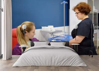 A nurse measures pressure with a young woman before taking a blood. Checkup of patient health in a modern laboratory clinic or hospital. Young adult girl donor is at the time of donation Wall mural