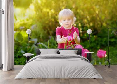 Cute little boy look at amazing purple and white peonies in sunny domestic garden Wall mural