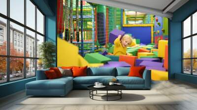 Cute little boy plays with soft cubes in the dry pool in play center. Kid playing on indoor playground in foam rubber pit in trampoline. Wall mural