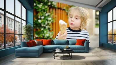 Happy little boy eating tasty ice cream cone outdoors during family stroll. Child have a snack on the go. Gelato is loved delicacy of kids. Sweets are unhealthy food for baby. Diabetes risk Wall mural