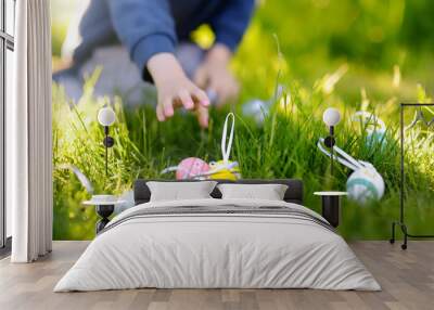 Little boy hunting for easter egg in spring garden on Easter day. Focus on multicolor eggs. Wall mural