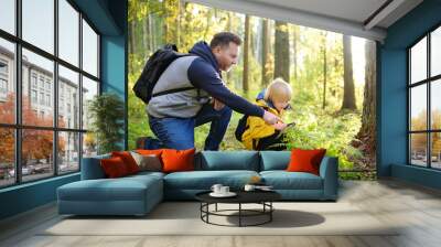 School boy and his father hiking together and exploring nature with magnifying glass. Child with his dad spend quality family time together in the sunny summer forest. Wall mural