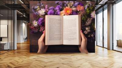 A person holding an open book in front of a bunch of flowers Wall mural