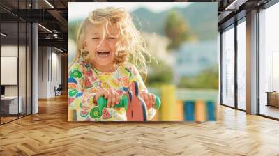 sunny summer day excited happy smiling face child girl in yellow dress play on colored wooden children playground in kindergarten Wall mural