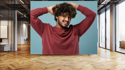 Annoyed young Asian man suffering from annoying itch or dandruff, scratching head on blue background Wall mural