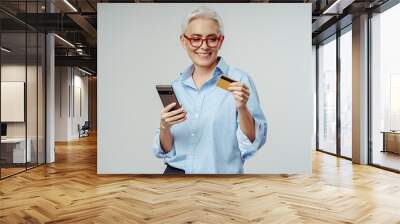 Beautiful gray haired senior woman holding credit card, mobile phone shopping Wall mural