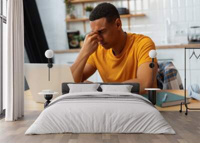 Depressed sad Latin man working at home, using laptop, eyes closed, having migraine, having bad news Wall mural