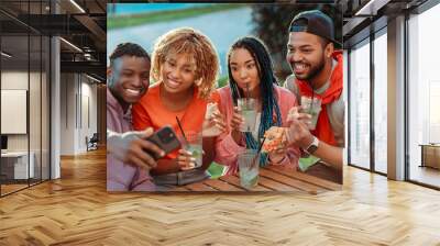 Group of smiling stylish African American  friends taking selfie, eating pizza, drinking lemonade sitting together in modern cafe  Wall mural