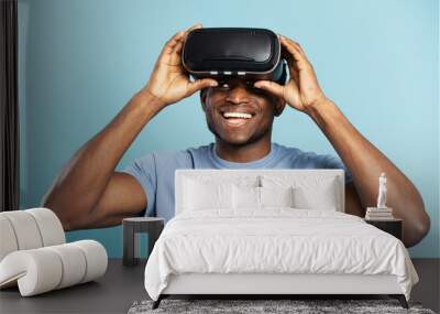 Handsome, nigerian man wearing VR glasses and playing video game, isolated on blue background Wall mural