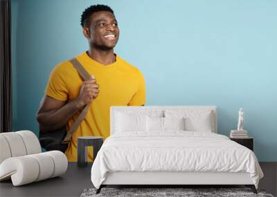 Handsome smiling African American student holding backpack looking away isolated on blue background, education concept. Portrait of happy handsome tourist Wall mural