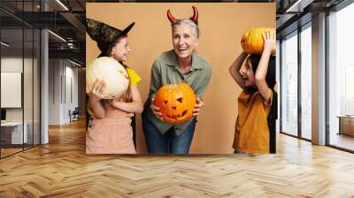 Happy grandmother and two little girls wearing halloween costumes holding pumpkins and smiling Wall mural