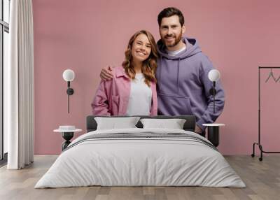 Portrait of attractive smiling couple hugging isolated on pink background. Happy bearded man and beautiful woman wearing stylish casual clothing looking at camera in studio Wall mural