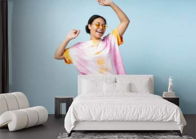 Portrait of beautiful happy African American woman dancing wearing trendy tie dye t shirt isolated on blue background. Smiling  stylish fashion model having fun posing for picture in studio  Wall mural