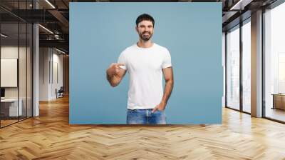 Portrait of handsome, smiling, bearded man wearing stylish white t shirt, pointing finger, mock up Wall mural