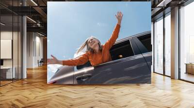 Portrait of happy senior gray haired woman sitting inside new car, holding hands up, having fun. Positive lifestyle, freedom, road trip, vacation concept Wall mural