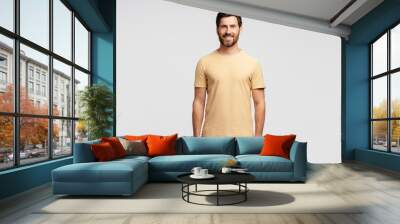 Portrait of smiling handsome bearded man, hipster wearing blank t shirt looking at camera isolated on gray background. Happy successful fashion model posing for pictures, studio shot. Mockup Wall mural