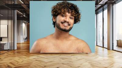 Portrait of smiling Indian man with naked torso after shower standing looking in mirror isolated on blue background. Attractive young male, concept of body care, beauty procedures Wall mural