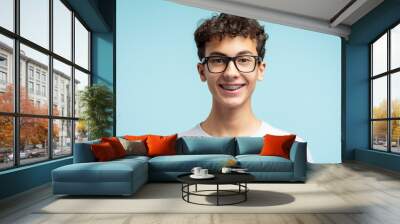 Portrait of smiling smart school boy with braces wearing glasses isolated on blue background. Education concept Wall mural