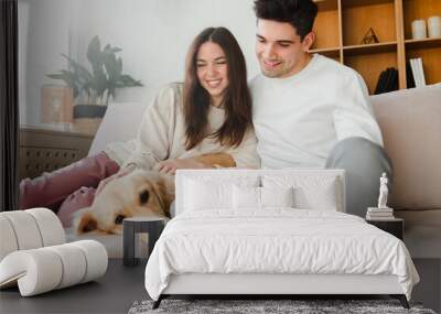 Portrait of smiling young couple attractive man and woman hugging golden retriever looking at camera Wall mural