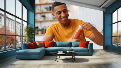 Portrait of young African American man wearing stylish yellow t shirt holding bottle of smoothie Wall mural