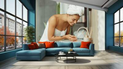 Portrait of young cheerful woman wearing white towel after shower, washing face with water Wall mural