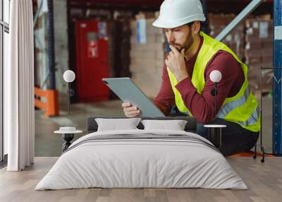 Serious, pensive, bearded man, foreman wearing hard hat and workwear, using digital tablet, thinking Wall mural