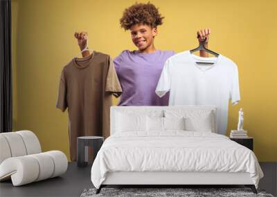 Smiling, attractive African American boy holding two t shirts white and purple, looking at camera Wall mural