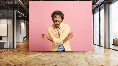 Smiling, attractive Indian man with curly hair smiling and posing on pink background Wall mural