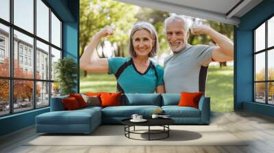 Smiling, attractive senior athletic couple flexing muscles in park, looking at camera outdoors Wall mural