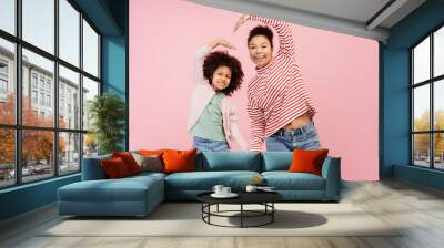 Smiling mother and her daughter posing in studio and making heart by their hands, isolated on pink Wall mural