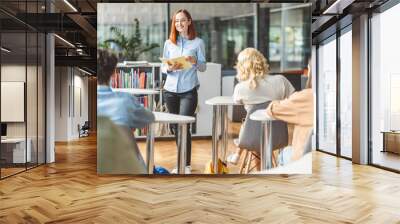 Smiling school teacher standing, explaining something to smart teenage students, exam preparing Wall mural