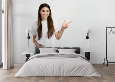 Smiling  teenage girl wearing white t shirt and stylish jeans, pointing finger at copy space, place for text. Happy teen showing to empty place, advertisement. Shopping concept  Wall mural