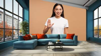 Young, beautiful Asian woman smiling and showing stop gesture with hand on beige background Wall mural