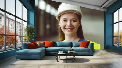 Young, smiling, beautiful woman wearing white hard hat and workwear looking at camera Wall mural