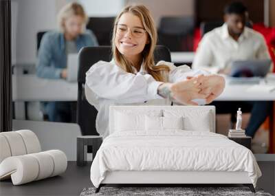 Young, smiling businesswoman stretching arms at office desk, break Wall mural