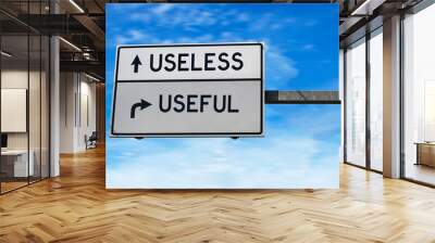 Road sign with words useless versus useful. White two street signs with arrow on metal pole on blue sky background. Wall mural