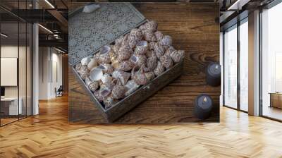 Closeup shot of the shells in the grey metallic box surrounded with two candles on the wooden table Wall mural